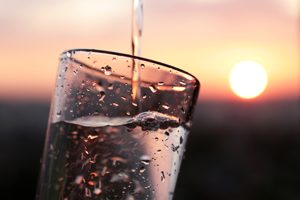 Pouring,Clean,Water,Into,Drinking,Glass,On,Sunset,Blurred,Background,